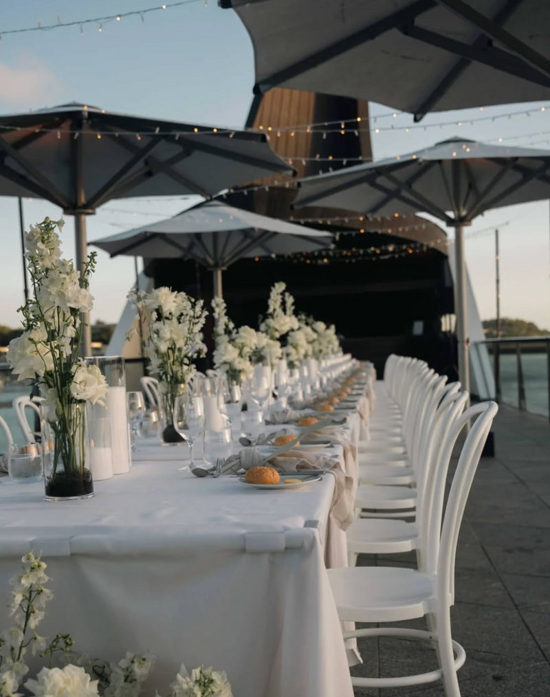 A bright and inviting outdoor hospitality setting with neatly arranged tables, white tablecloths, and umbrellas.